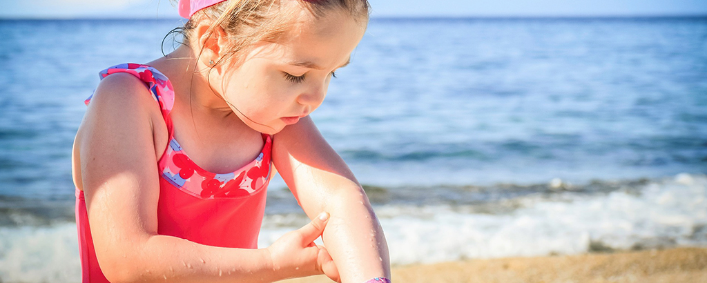 kid with red swim suite looking at her arm with sea in the background
